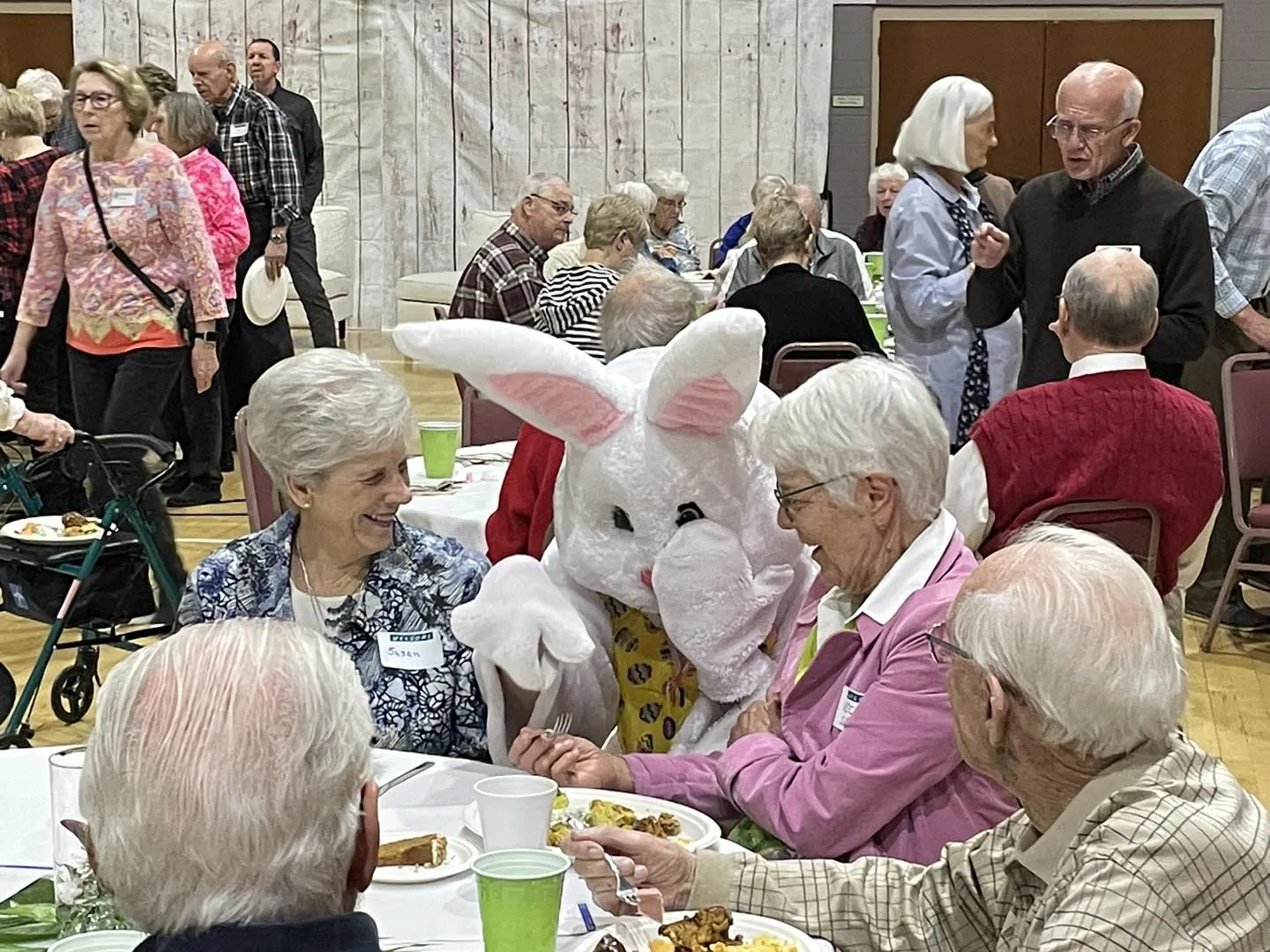 Older adults enjoying a social gathering at a church event with a festive mascot present.